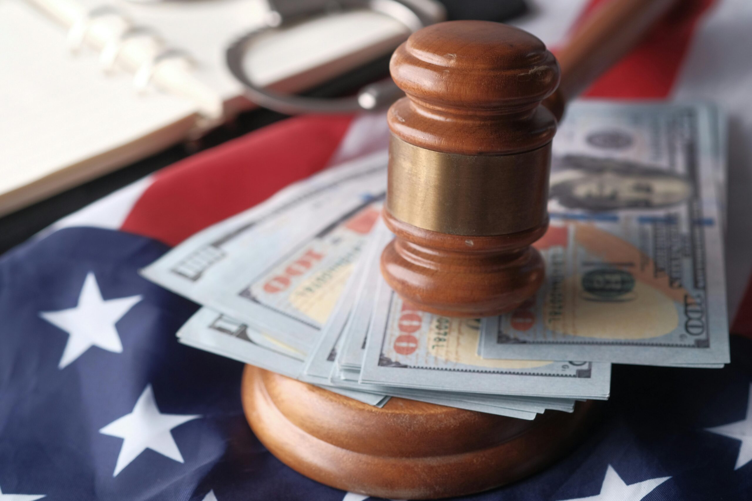 Home Close-up of a judge's gavel resting on US dollar bills and an American flag, symbolizing justice and finance.